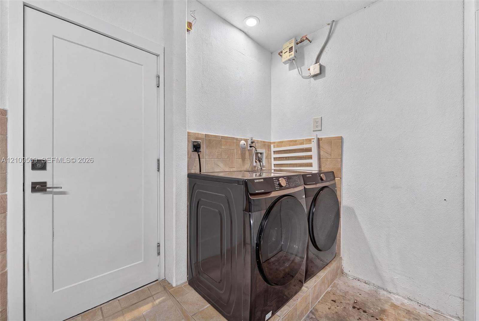 7721 NW 201st Terrace, Hialeah, FL 33015 Laundry area featuring a tile backsplash, recessed ceiling lighting, and a solid-core interior door with brushed metal hardware