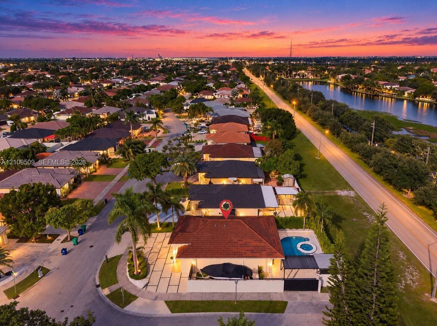 7721 NW 201st Terrace, Hialeah, FL 33015 Aerial perspective of a corner-lot property featuring a tile roof, an integrated swimming pool and spa, a paved driveway with turf accents, and perimeter wall fencing