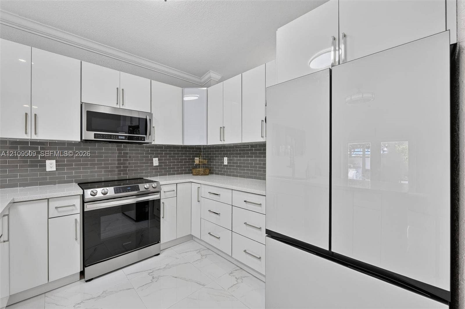 7721 NW 201st Terrace, Hialeah, FL 33015 Kitchen featuring high-gloss white cabinetry, light-toned stone-finish countertops, grey subway tile backsplash, stainless steel appliances, and large-format white tile flooring with grey veining