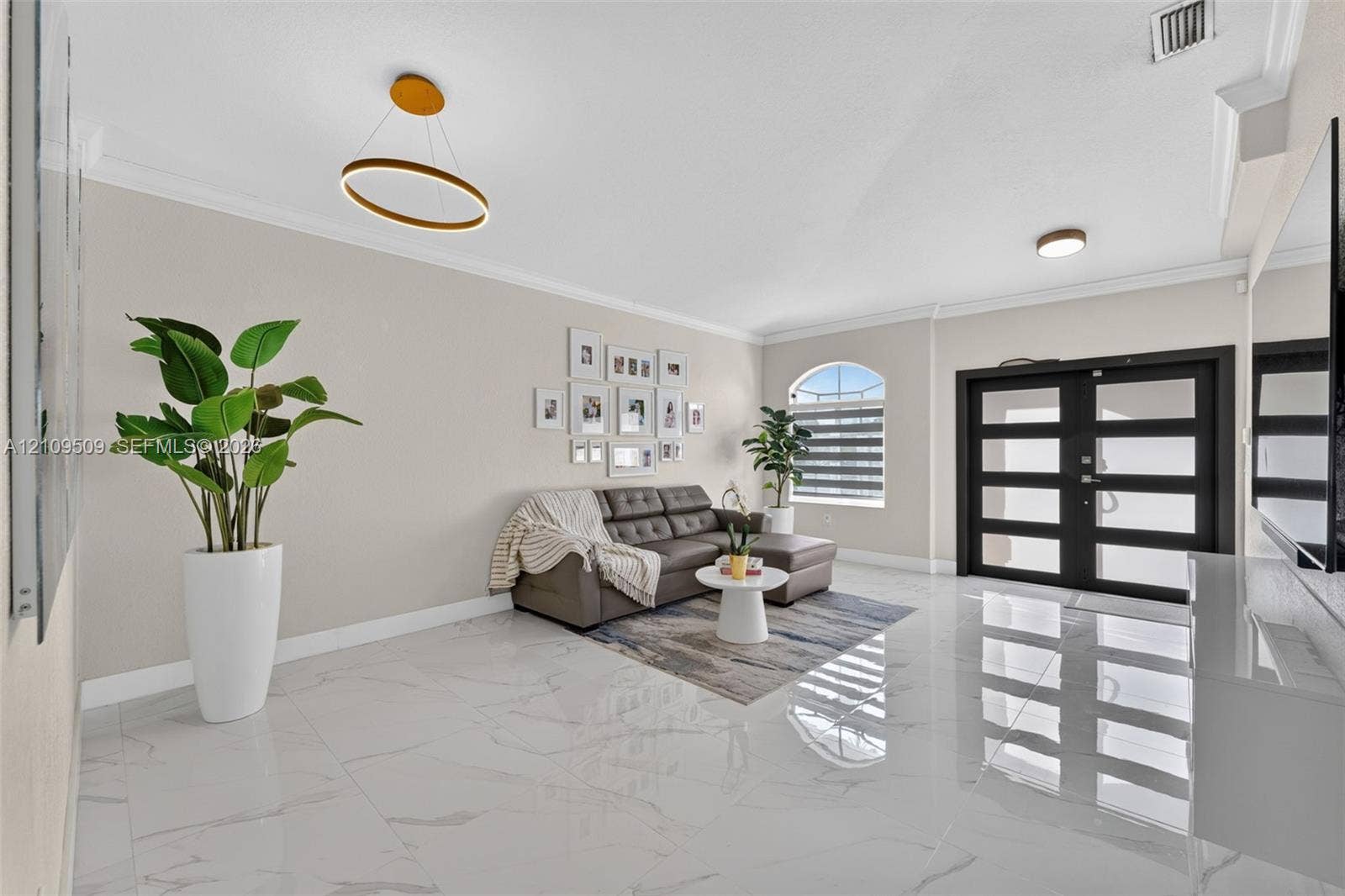 7721 NW 201st Terrace, Hialeah, FL 33015 Large-format polished tile flooring, double-door entry with glass panels, crown molding, modern ring-style pendant lighting, and an arched window