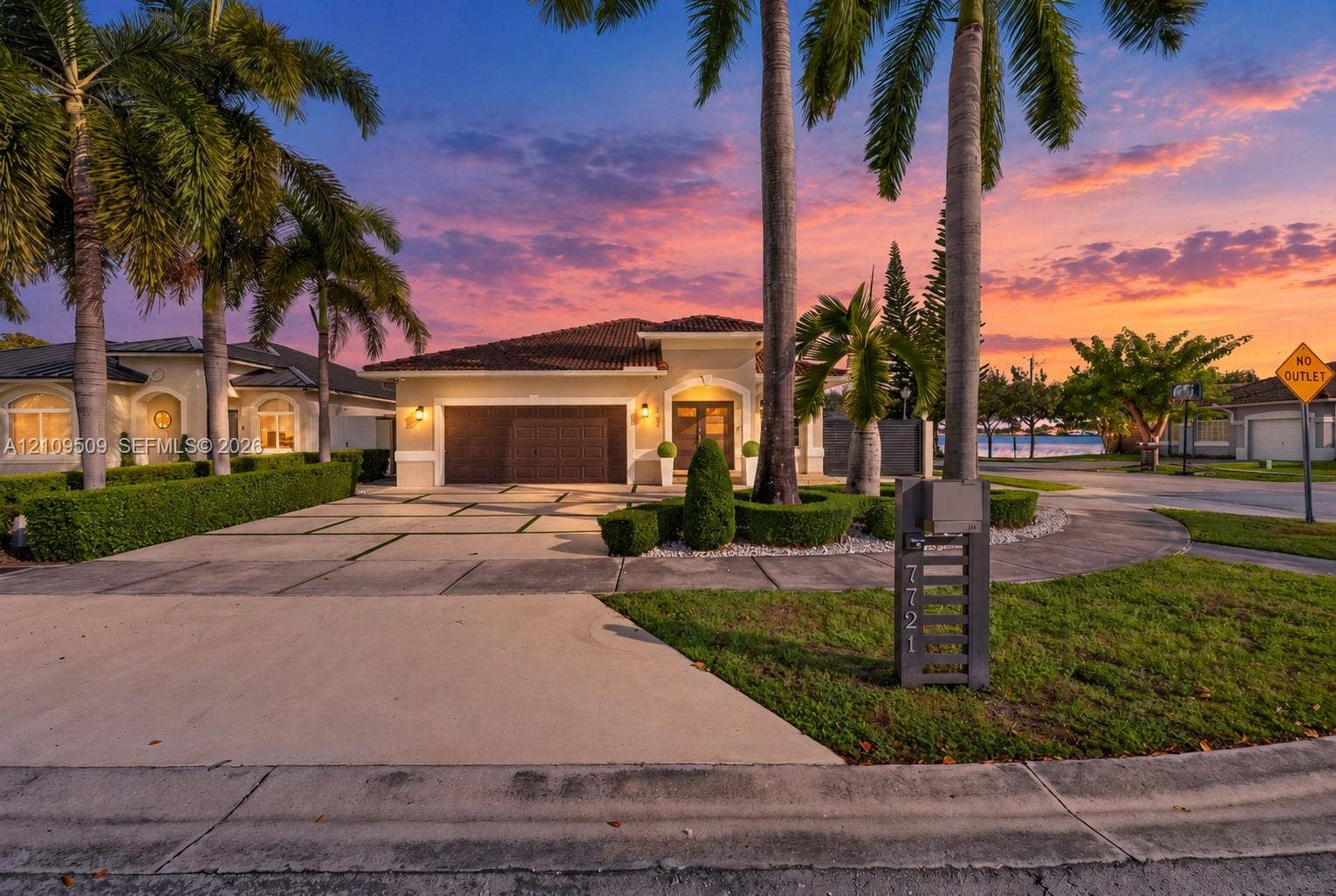 7721 NW 201st Terrace, Hialeah, FL 33015 Stucco exterior with a tiled roof, multi-car garage, expansive concrete driveway with geometric lawn inlays, and mature palm tree landscaping
