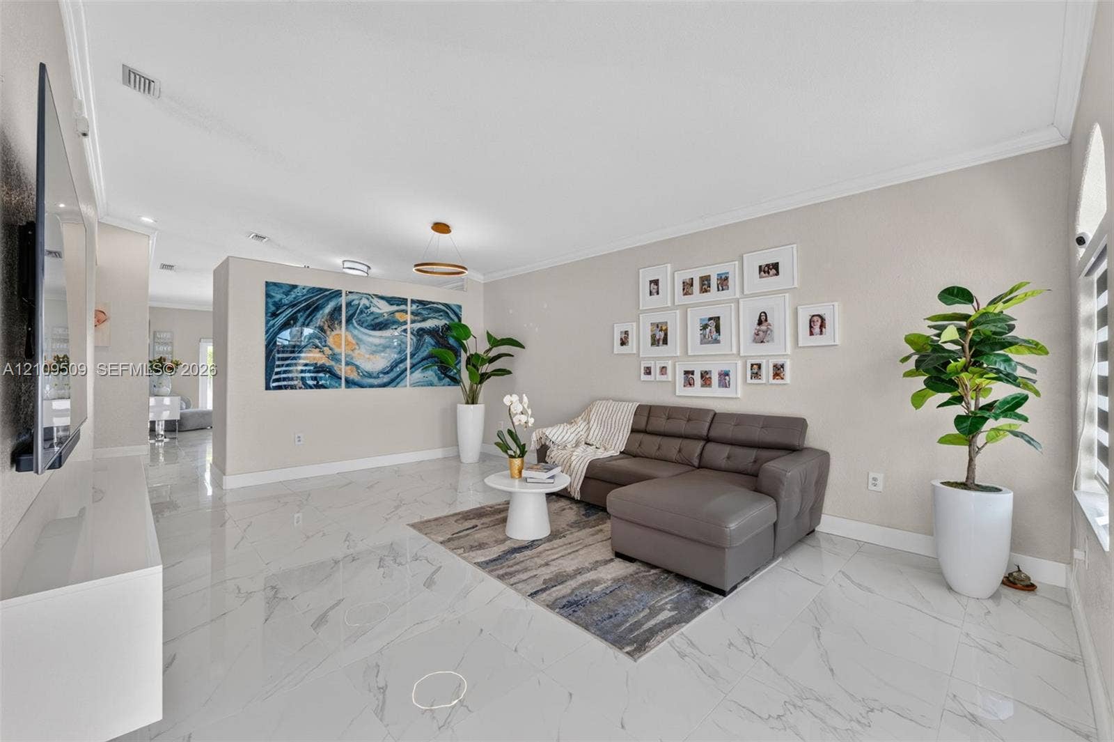 7721 NW 201st Terrace, Hialeah, FL 33015 Open floor plan living area featuring polished stone-finish floor tiling, crown molding, recessed lighting, and a modern tiered pendant light fixture