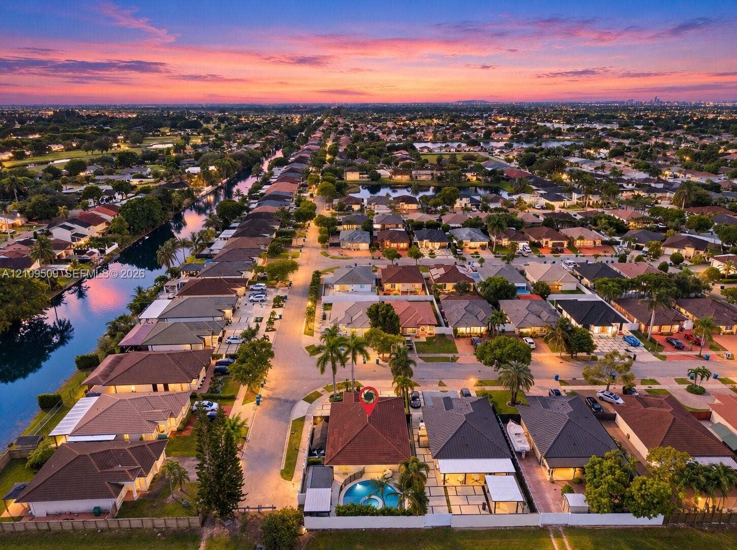 7721 NW 201st Terrace, Hialeah, FL 33015 Aerial perspective of a residential property featuring a tiled roof, an in-ground swimming pool, a stone-paver patio, and mature palm trees