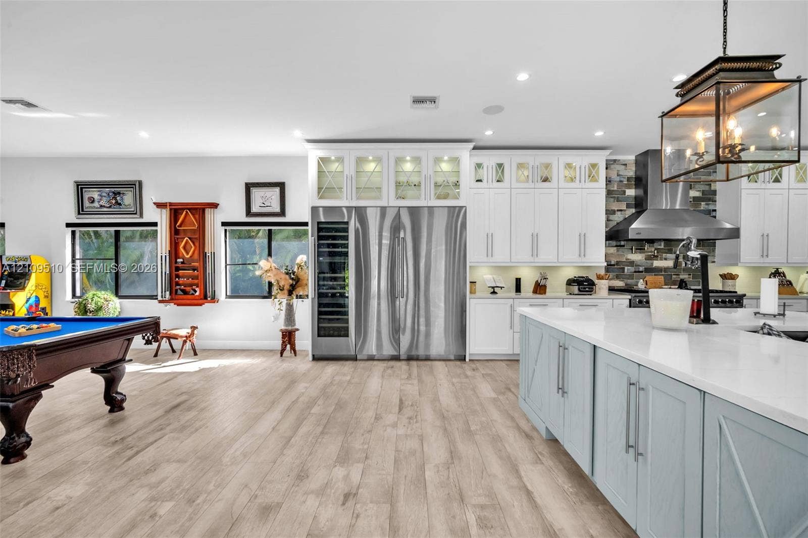 5760 SW 188th Avenue, Southwest Ranches, FL 33332 Kitchen featuring custom white cabinetry with glass-front uppers, a stainless steel side-by-side refrigerator, a built-in wine cooler, a stone tile backsplash, and a central island with a quartz countertop