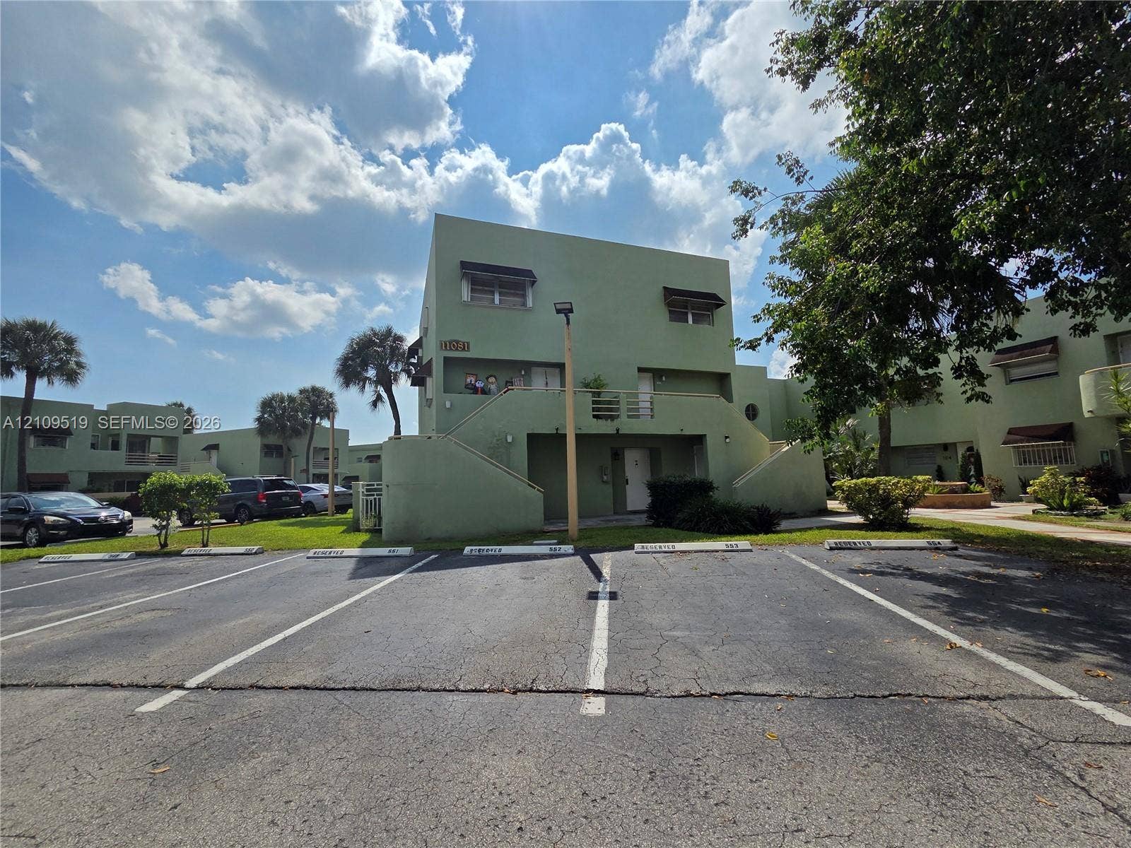 11081 NW 7th Street, #101-14, Miami, FL 33172 Exterior featuring a stucco facade, external staircase, individual assigned parking stalls, and mature landscaping