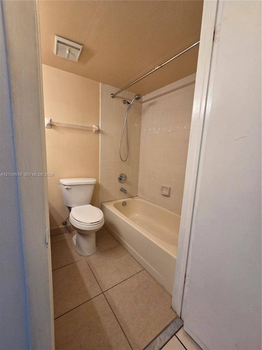 11081 NW 7th Street, #101-14, Miami, FL 33172 Bathroom featuring a porcelain toilet, a bathtub with a wall-mounted handheld shower fixture, tiled shower surround, and ceramic tile flooring
