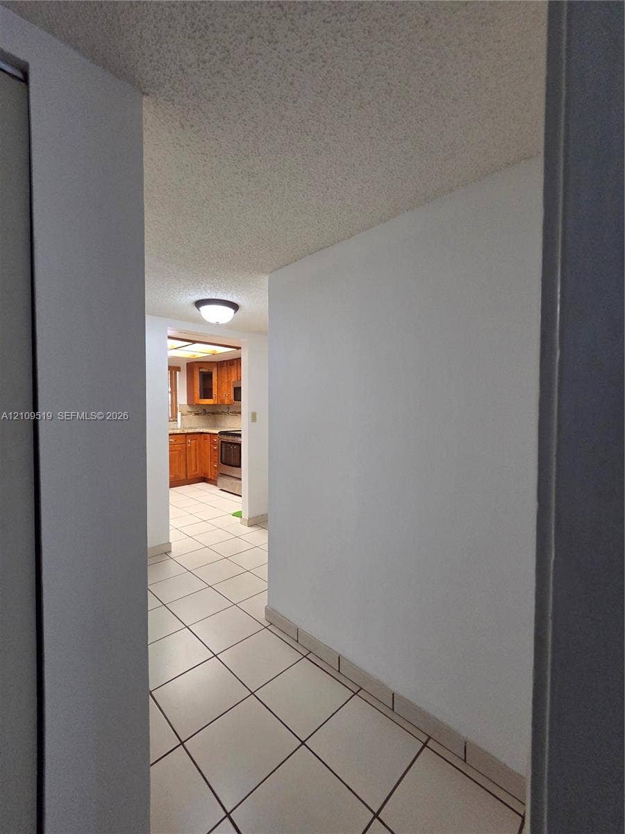 11081 NW 7th Street, #101-14, Miami, FL 33172 Ceramic tile flooring, flush-mount ceiling lighting, and wooden cabinetry with integrated appliances view from hallway