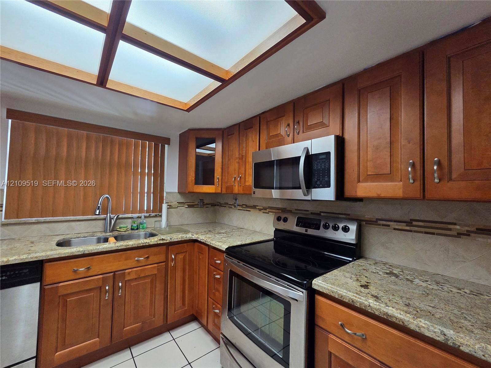 11081 NW 7th Street, #101-14, Miami, FL 33172 Kitchen featuring stained wood cabinetry, stone-surface countertops, built-in stainless steel appliances, a tile backsplash, and a recessed ceiling skylight