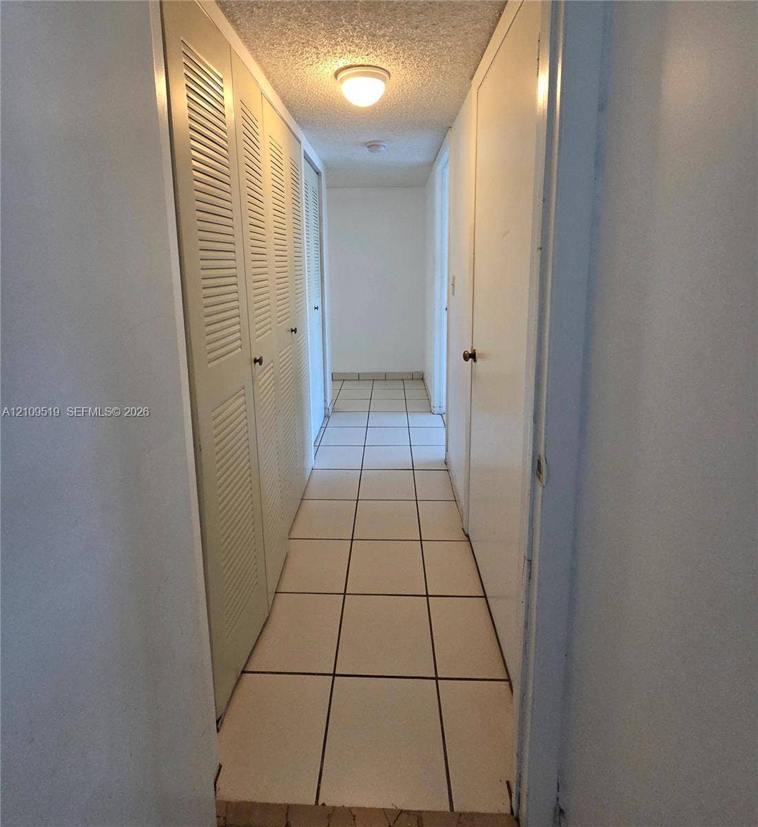 11081 NW 7th Street, #101-14, Miami, FL 33172 Hallway featuring light-colored tile flooring, multiple louvered-style closet doors, solid-panel doors, and a ceiling-mounted light fixture
