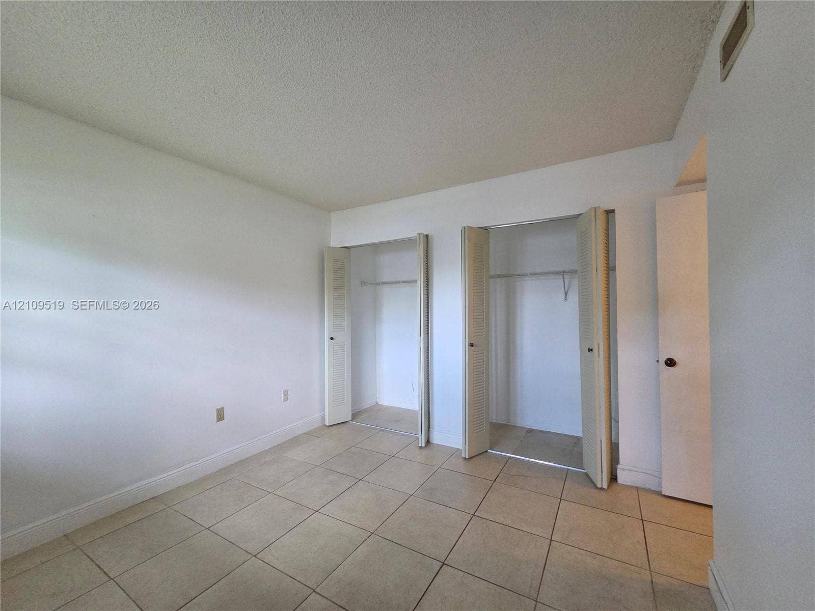 11081 NW 7th Street, #101-14, Miami, FL 33172 Room featuring neutral tile flooring, two closets with bi-fold doors, and a separate doorway entrance