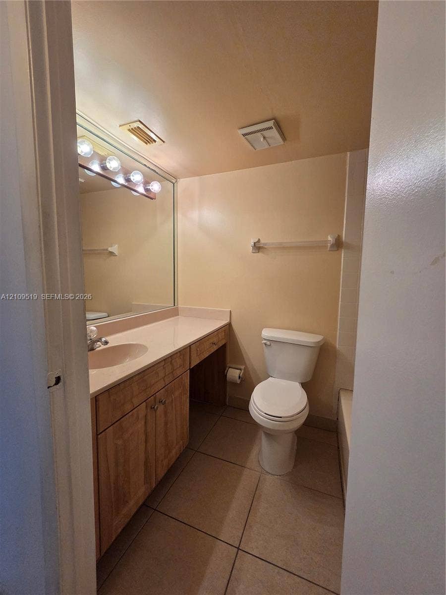 11081 NW 7th Street, #101-14, Miami, FL 33172 Bathroom featuring a vanity with wood-finish cabinetry, a solid surface integrated countertop, a full-width mirror with multi-bulb light fixture, and tile flooring
