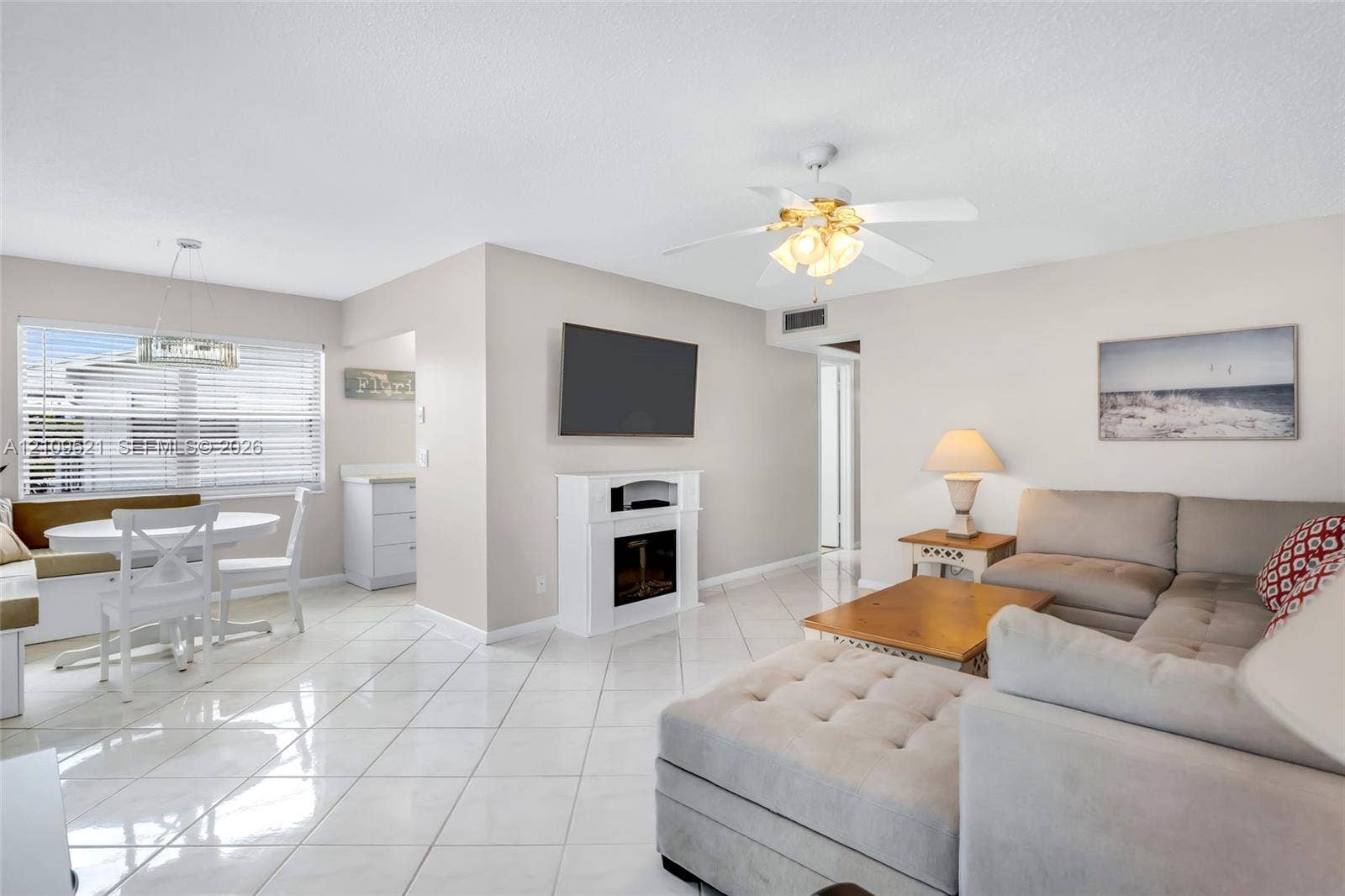 Living area featuring large-format diagonal tile flooring, a white built-in fireplace, a ceiling fan with integrated lighting, and multiple windows with horizontal blinds