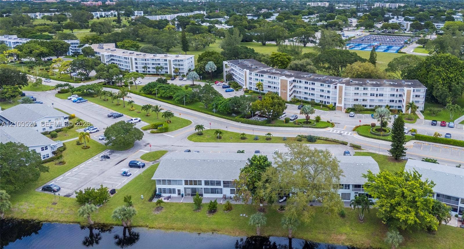 Aerial perspective of multi-story residential buildings featuring low-pitch roofing, expansive grounds, integrated parking areas, and waterfront positioning
