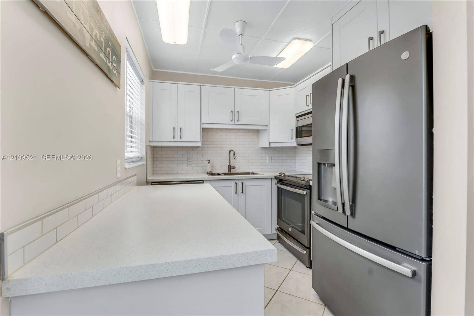 Kitchen featuring white cabinetry, subway tile backsplash, solid surface countertops, stainless steel appliances, and tile flooring