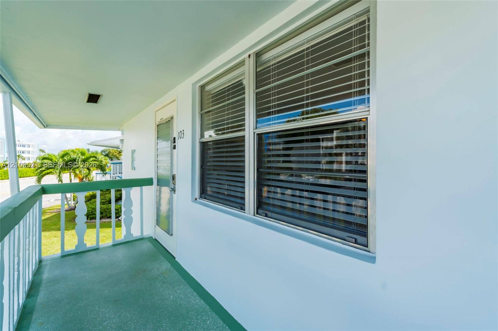 Covered exterior balcony featuring a solid-surface floor, painted railing with decorative posts, and horizontal sliding windows