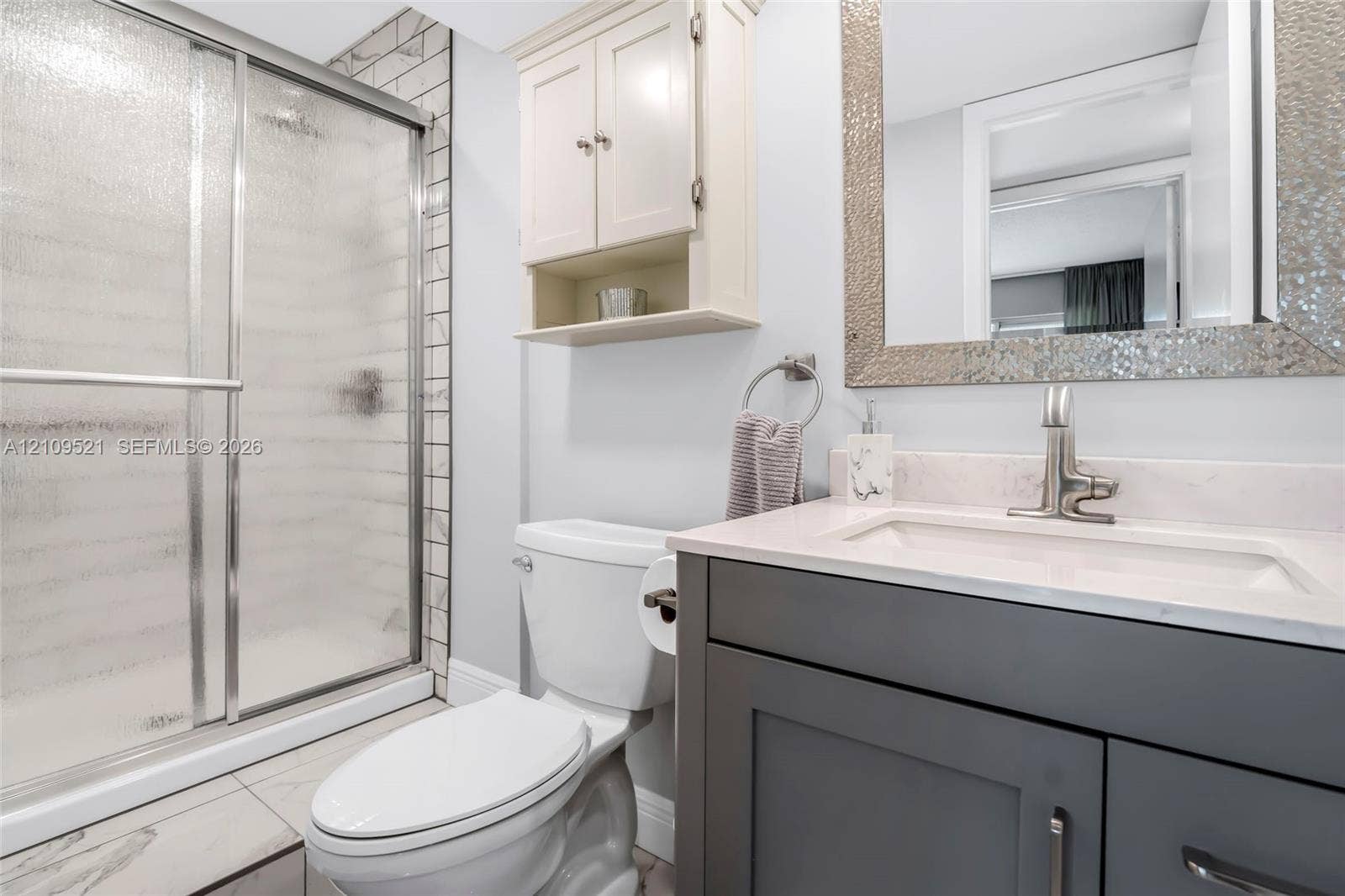 Bathroom featuring a grey vanity with a solid surface countertop, integrated sink, chrome faucet, glass-enclosed shower with tiled surround, and wall-mounted cabinetry