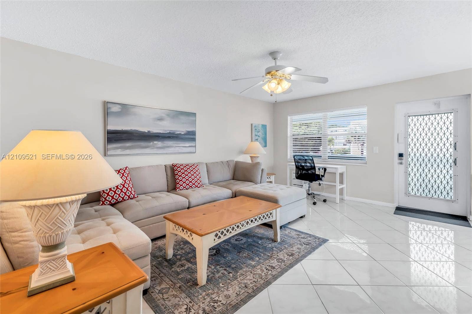 Living area featuring large-format ceramic tile flooring, a multi-blade ceiling fan with integrated lighting, and a window with horizontal blinds