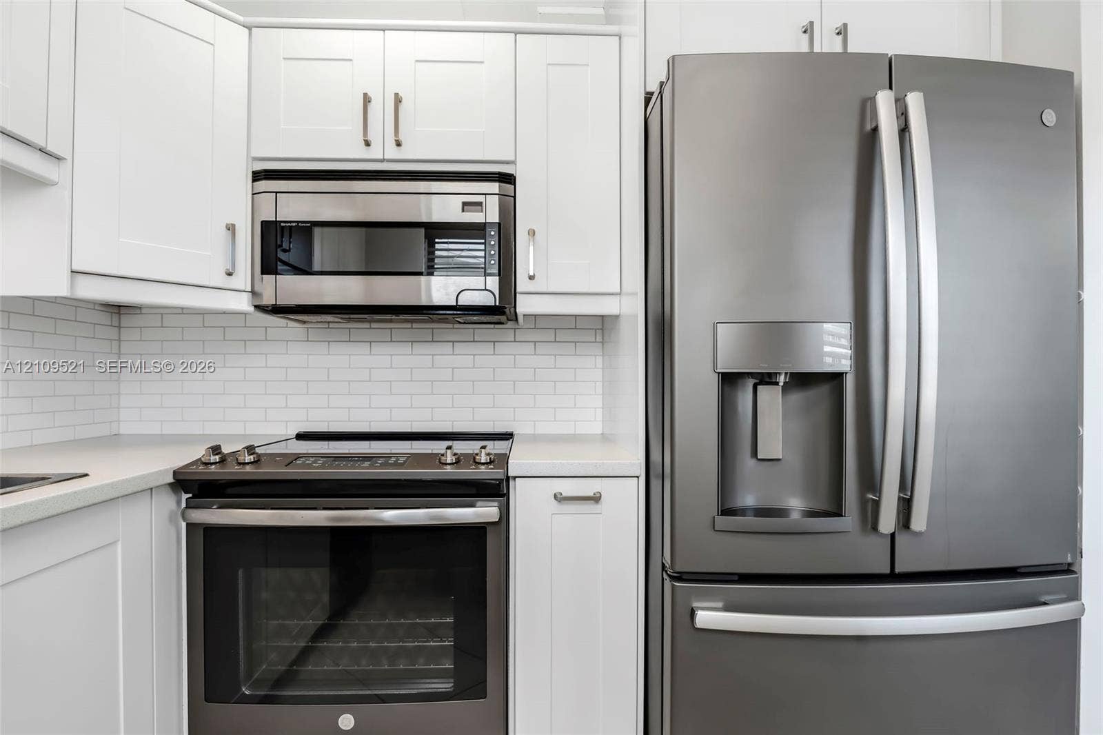 White shaker-style cabinetry, stainless steel microwave, matte-finish range, French-door refrigerator, and white subway tile backsplash