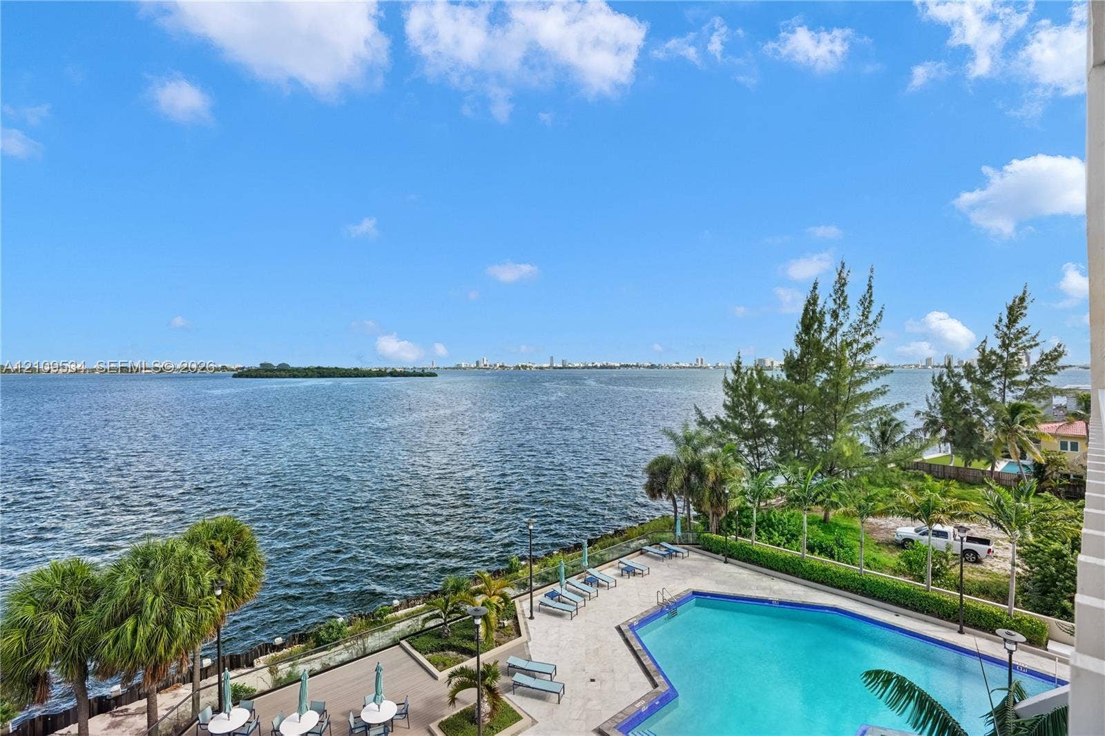 Outdoor swimming pool with tile decking and stone-paver surroundings, bordered by manicured landscaping and mature palm trees, featuring an expansive water view