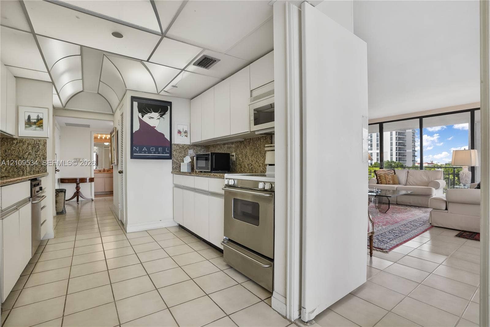 Kitchen featuring white flat-panel cabinetry, stone-finish countertops, stainless steel appliances, and a vaulted ceiling panel system