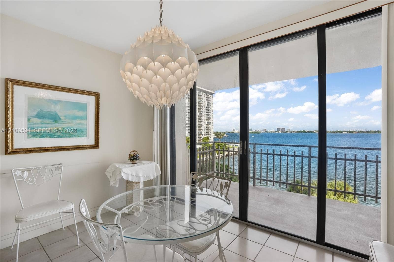 Floor-to-ceiling sliding glass doors, private balcony with metal railing, tile flooring, and decorative pendant light fixture