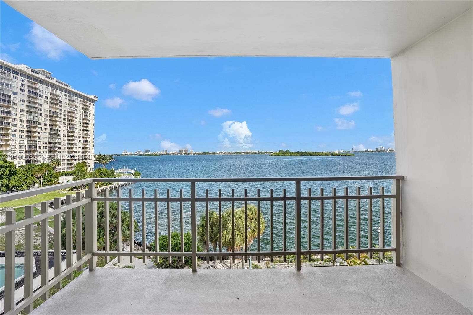 Covered balcony featuring metal railings and concrete flooring, overlooking expansive water scenery with coastal surroundings