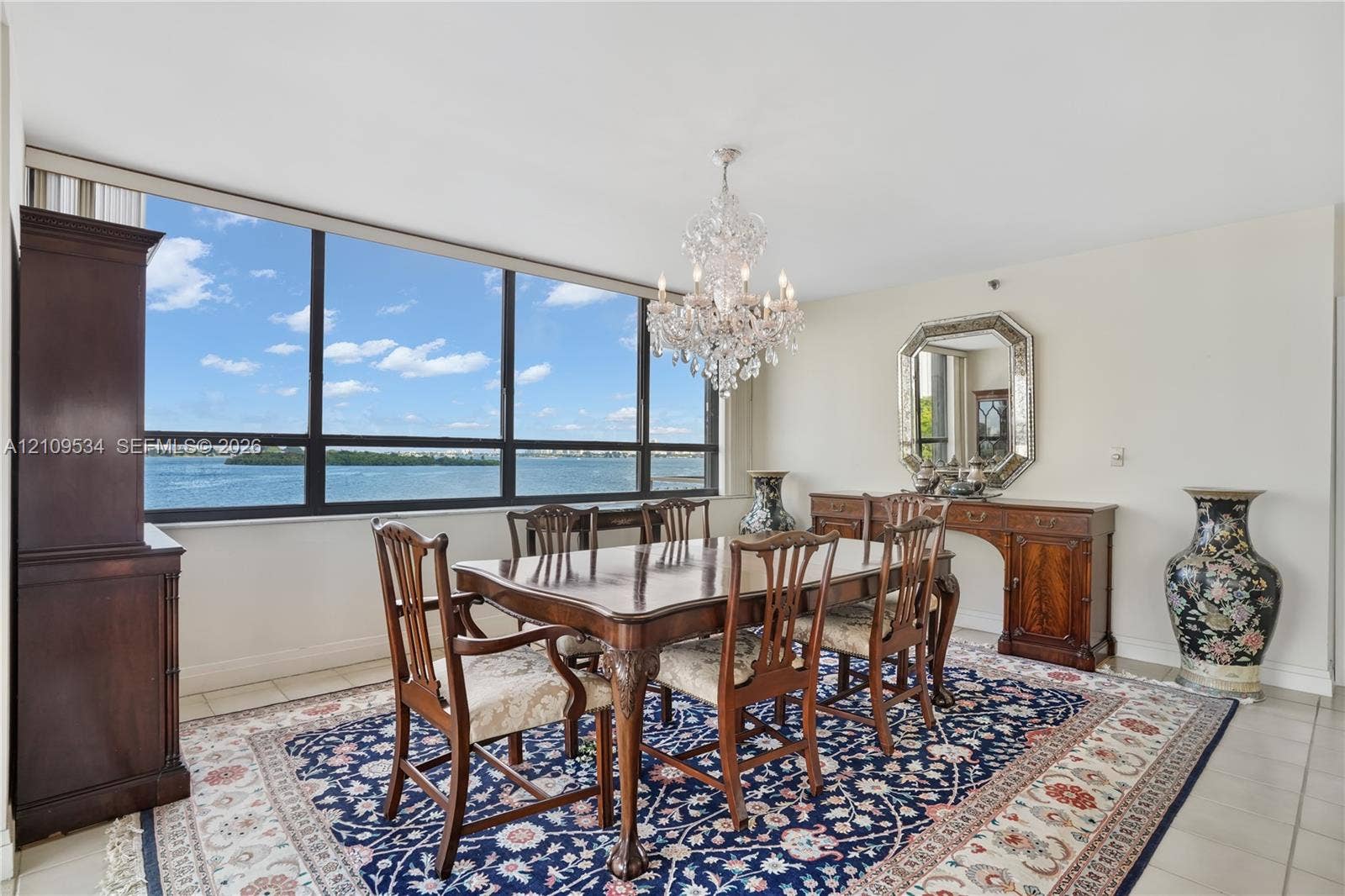 Floor-to-ceiling windows with water scenery, polished tile flooring, and a multi-tiered crystal chandelier