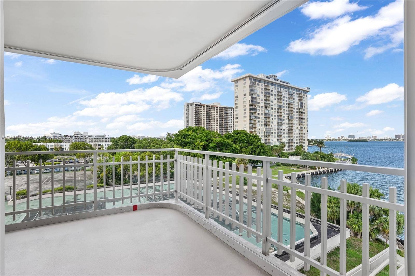 Covered balcony featuring white metal railings and concrete flooring, overlooking the waterfront