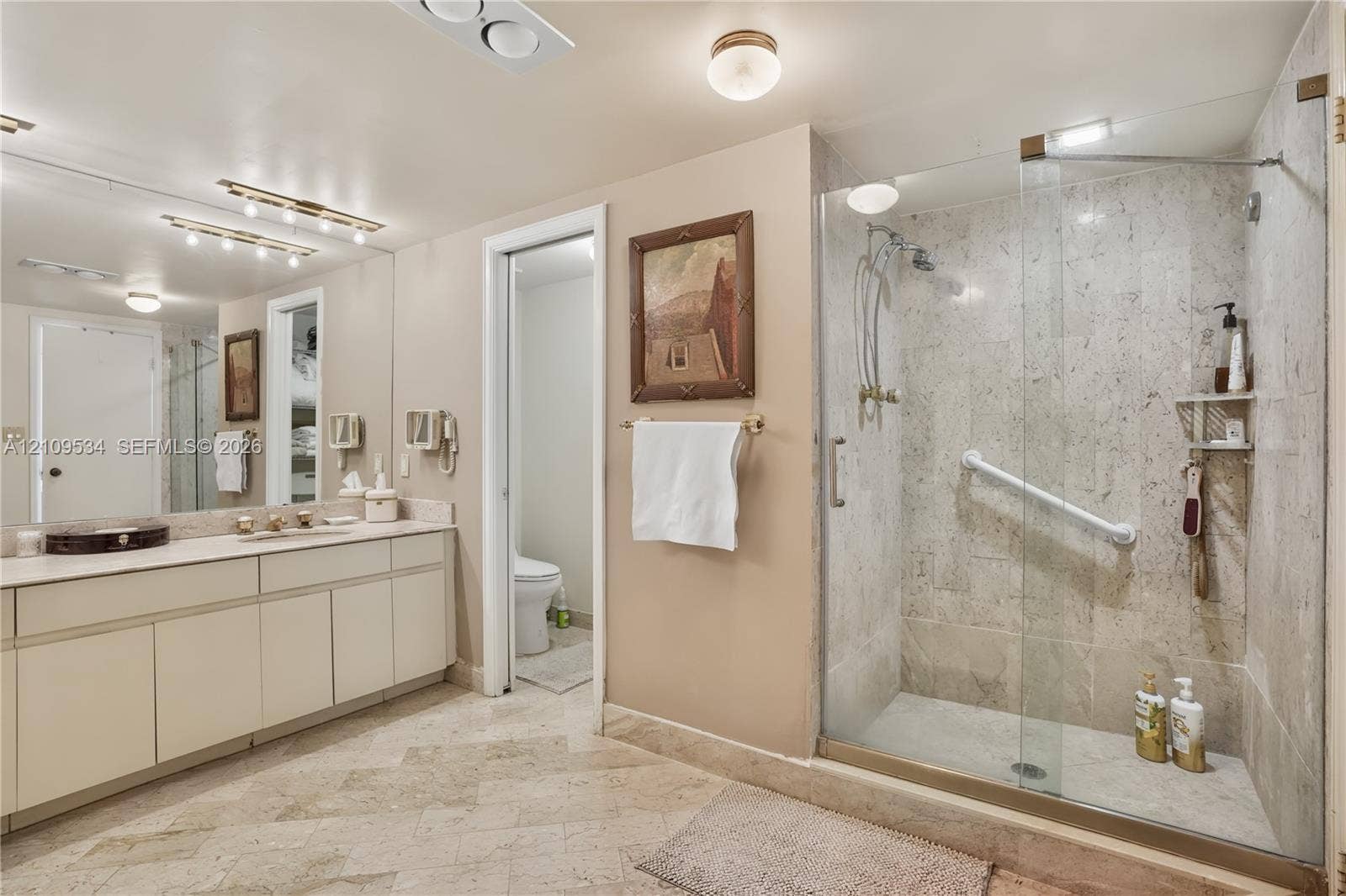 Bathroom featuring a dual-sink vanity with countertop, large wall-to-wall mirror, and stone-tile flooring