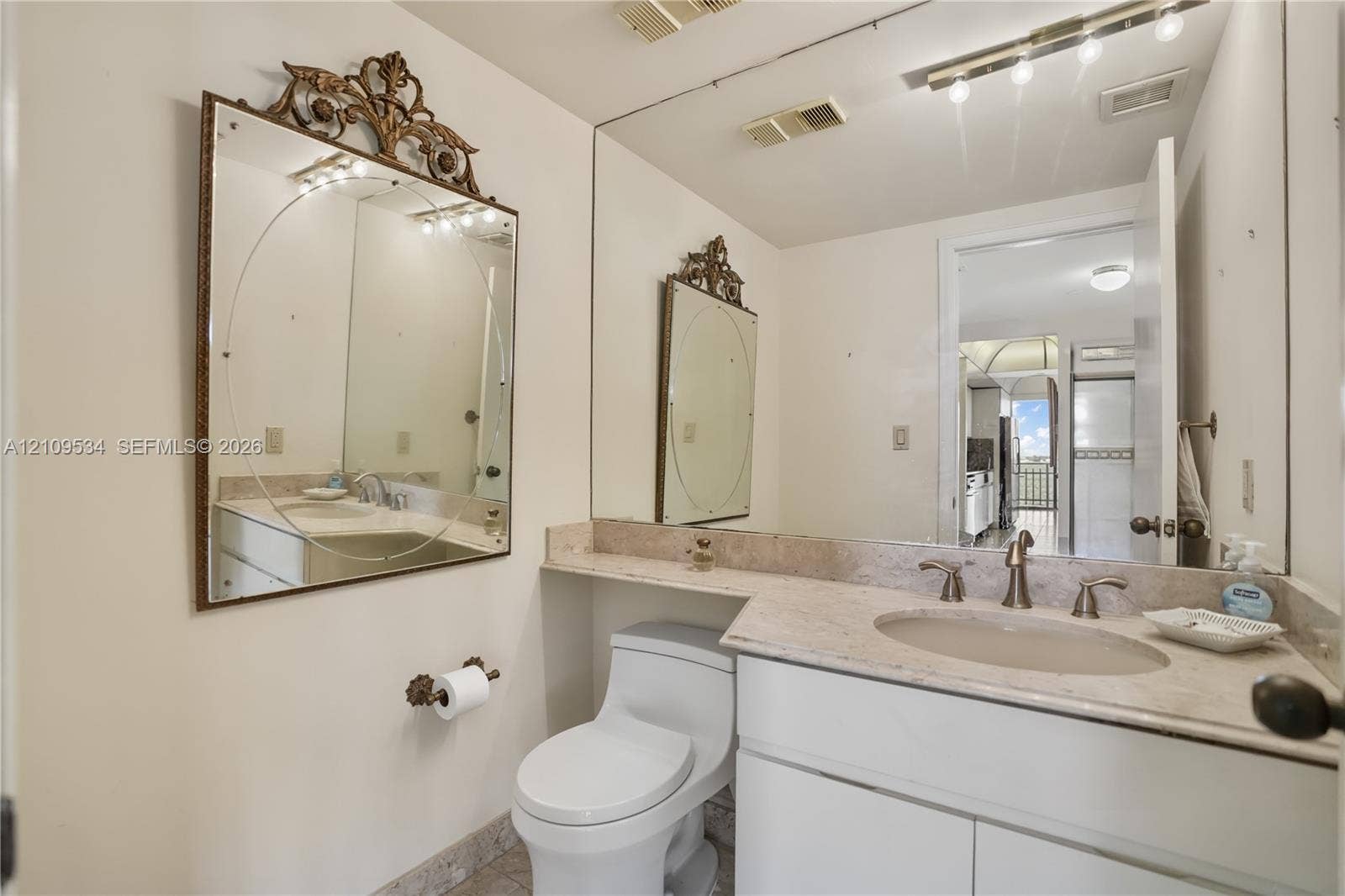 Bathroom featuring a stone-topped vanity with an integrated basin, white cabinetry, a large wall-mounted mirror, and an overhead vanity light fixture