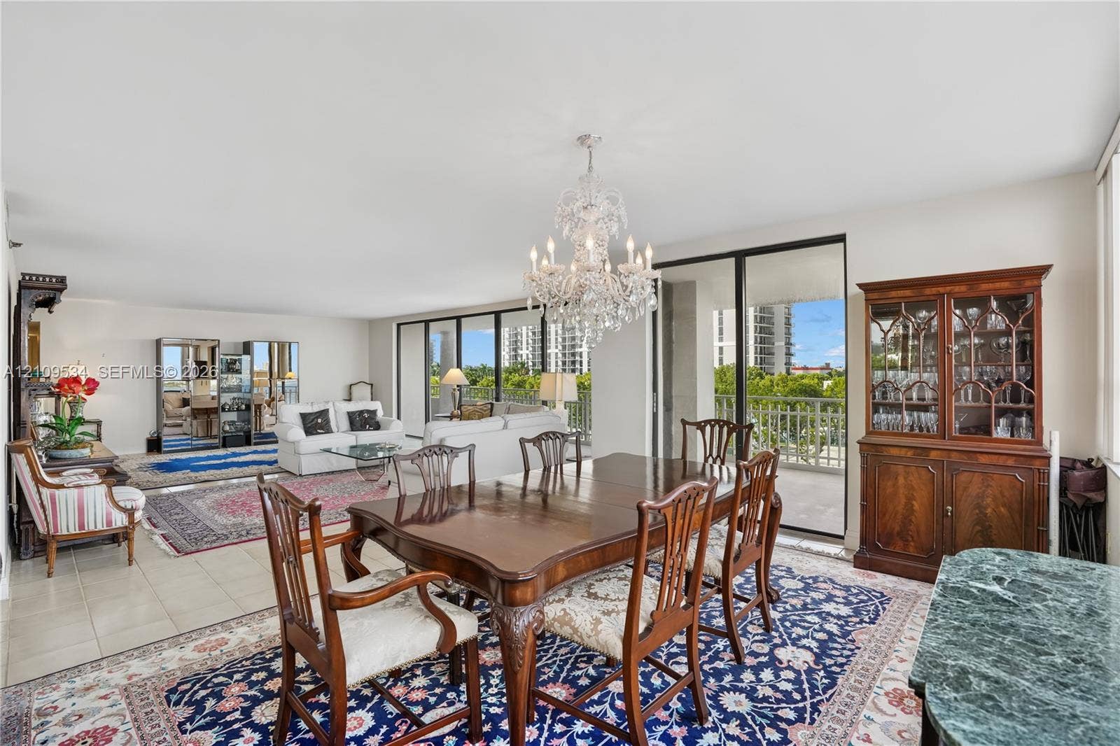 Open-concept living space featuring neutral tile flooring, a multi-tiered crystal chandelier, and large sliding glass doors providing outdoor access
