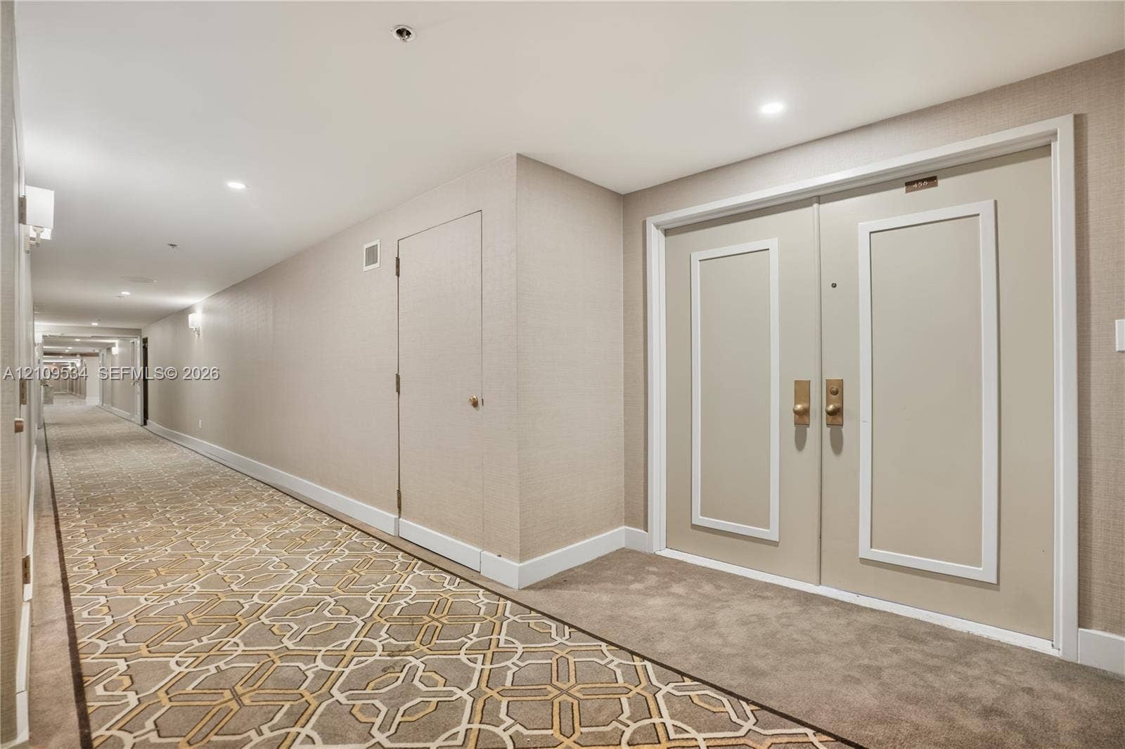 Hallway featuring recessed ceiling lighting, textured wall coverings, double doors with metallic hardware, and patterned carpeting