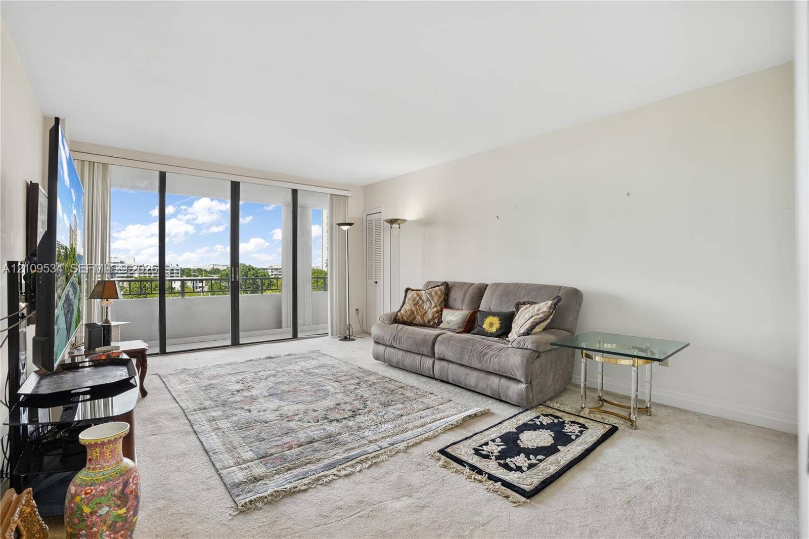 Living area featuring neutral carpeting, expansive floor-to-ceiling glass sliding doors, and a private balcony