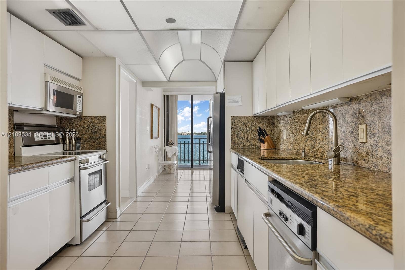 Kitchen featuring white cabinetry, stone-surface countertops, stainless steel appliances, ceramic tile flooring, and a barrel-vaulted ceiling