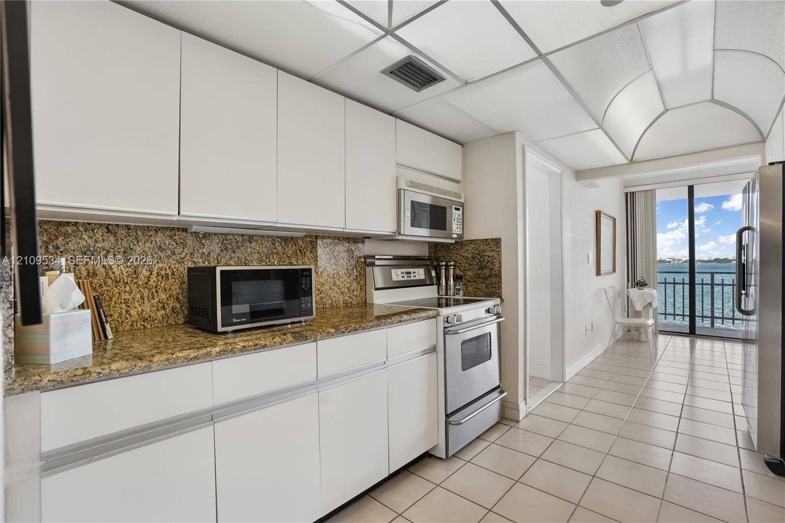 Kitchen featuring flat-panel cabinetry, stone countertops, stone backsplash, stainless steel appliances, and ceramic tile flooring