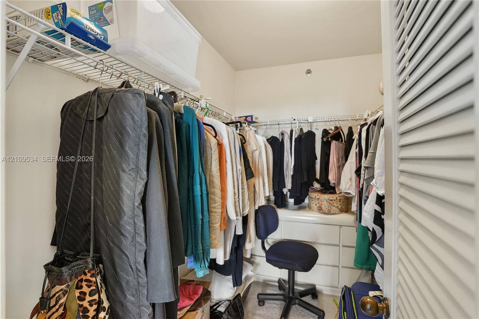 Walk-in closet featuring built-in white cabinetry, tiered metal shelving, and louvered door entry