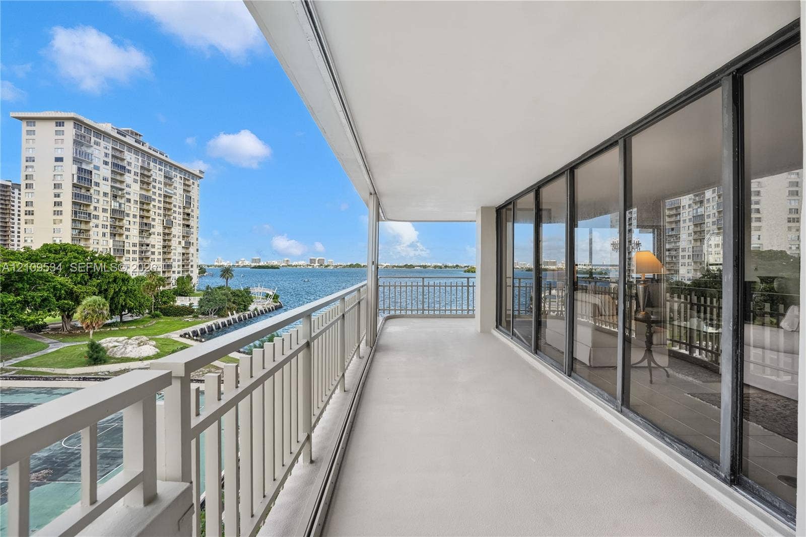 Covered balcony with floor-to-ceiling sliding glass doors, white metal railing, and water frontage