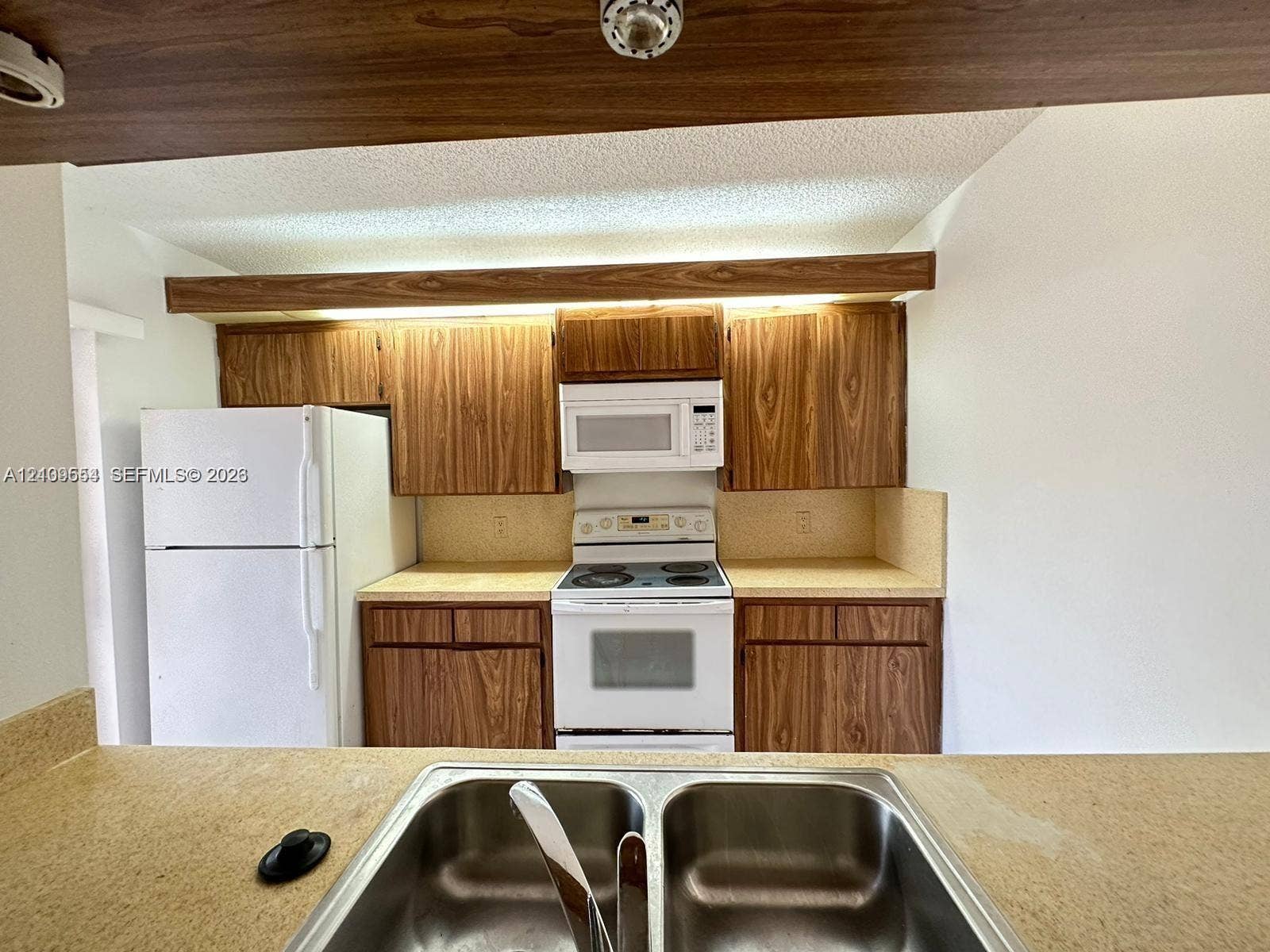 1802 18th Way, #1802, West Palm Beach, West Palm Beach, FL 33407 Kitchen featuring wood-finish cabinetry, a dual-basin stainless steel sink, solid-surface countertops, and a mounted microwave above the range
