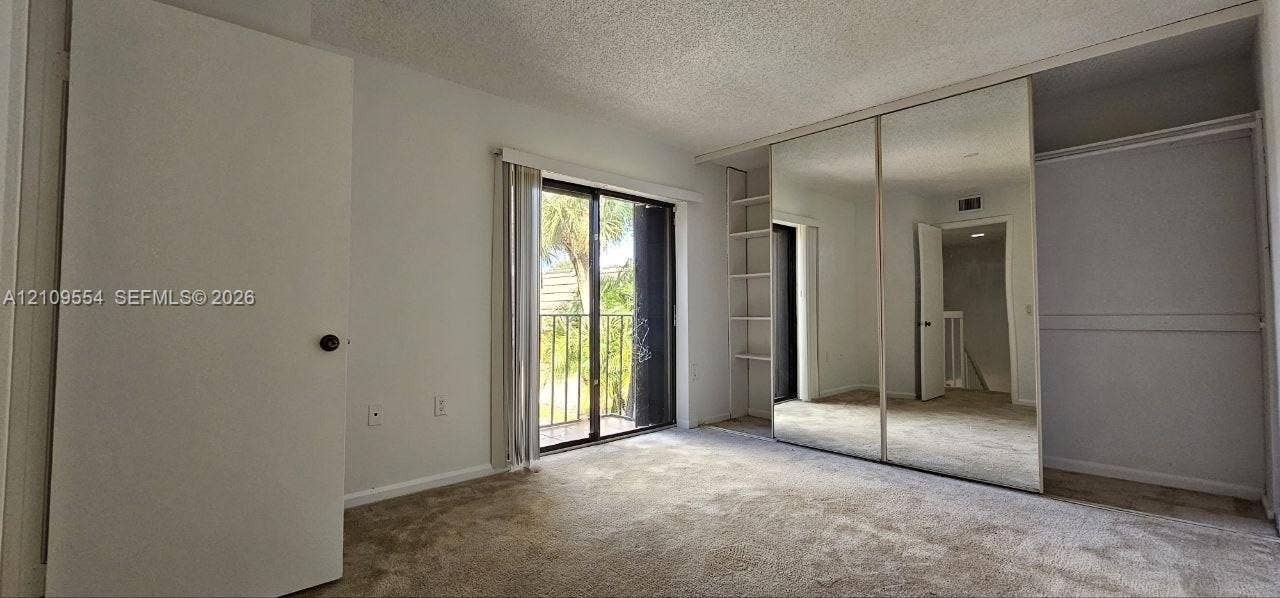 1802 18th Way, #1802, West Palm Beach, West Palm Beach, FL 33407 Interior space featuring carpeting, sliding glass doors to a balcony, mirrored closet doors, and built-in shelving