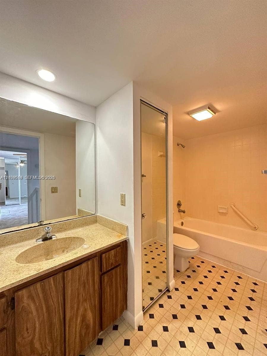 1802 18th Way, #1802, West Palm Beach, West Palm Beach, FL 33407 Bathroom featuring wood-finish cabinetry, stone-texture countertop with an integrated basin, wall-to-wall mirror, and geometric-patterned tile flooring