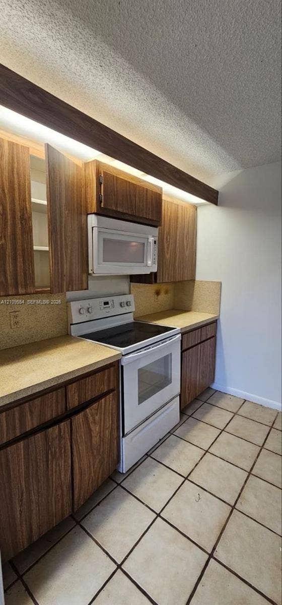 1802 18th Way, #1802, West Palm Beach, West Palm Beach, FL 33407 Kitchen featuring wood-finish cabinetry, white electric range with matching over-the-range microwave, solid-surface countertops, and ceramic tile flooring