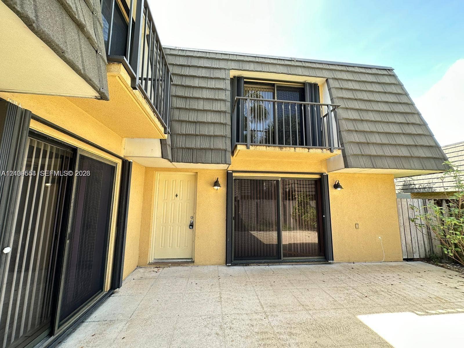 1802 18th Way, #1802, West Palm Beach, West Palm Beach, FL 33407 Exterior facade featuring a second-story balcony with metal railings, sliding glass patio doors, shingled mansard roof design, and a concrete patio