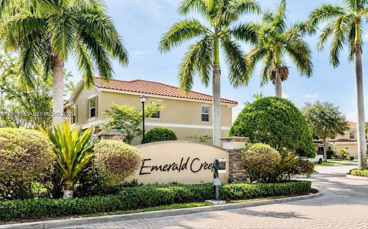 12444 Emerald Creek Court, Plantation, FL 33325 Stucco community entrance monument featuring stone pillar accents, paved roadway, mature palm trees, and manicured landscaping