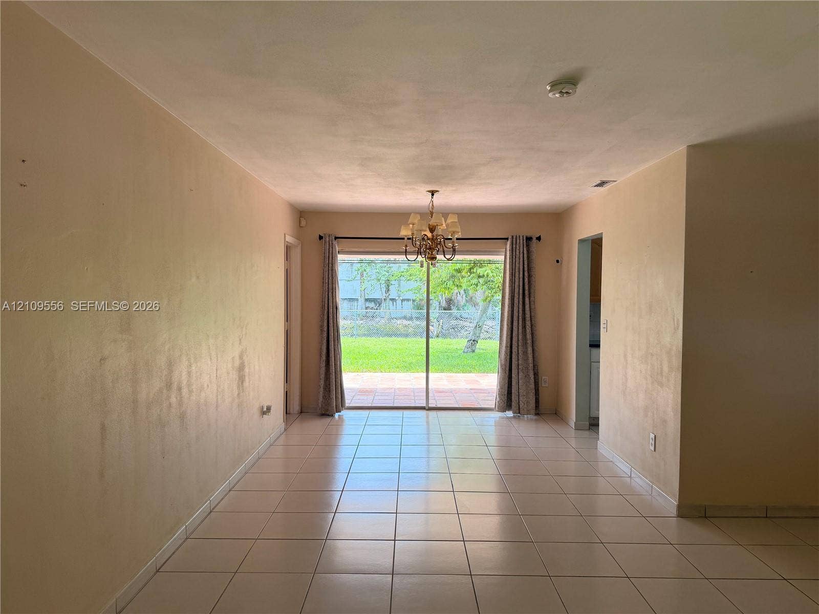 Large-format tile flooring, multi-arm chandelier, and sliding glass doors opening to an exterior patio