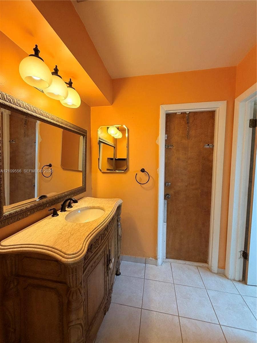 Vanity featuring an ornate carved wood-finish base, stone-texture countertop, under-mount oval sink, three-light fixture, and large rectangular framed mirror