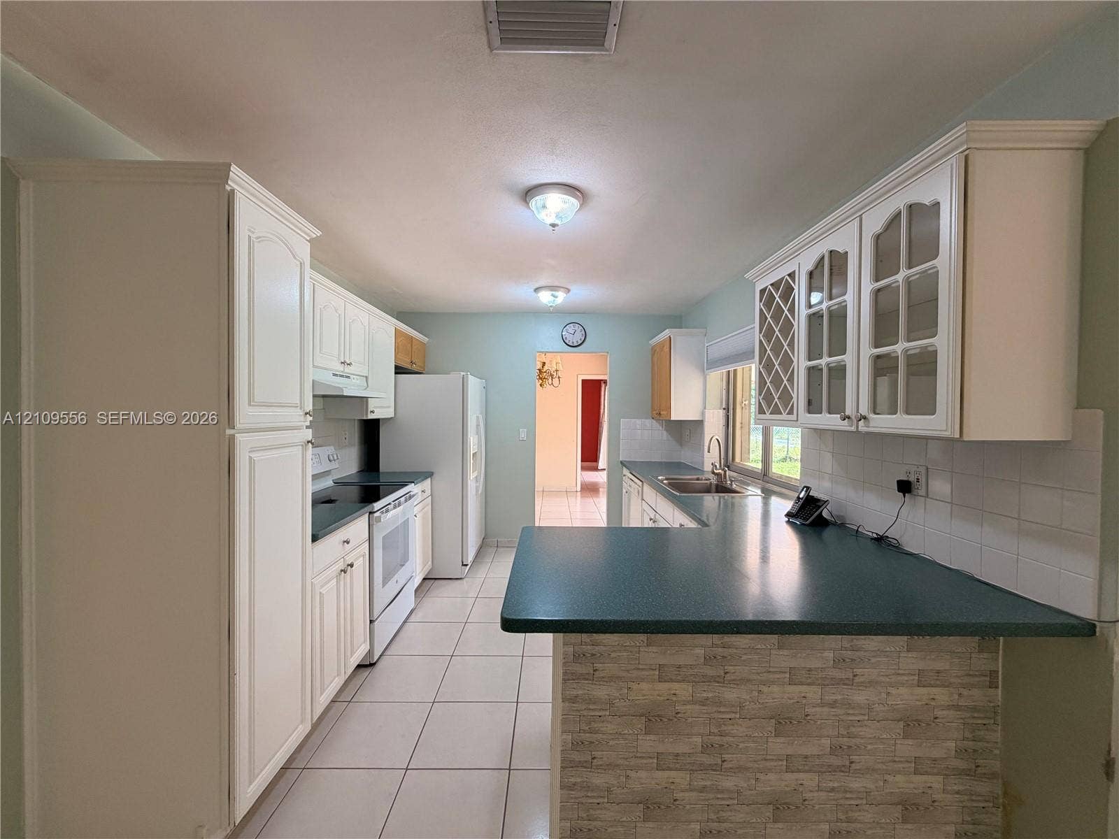 Kitchen featuring white cabinetry with glass-panel accents, integrated wine storage, contrasting countertops, and tile flooring