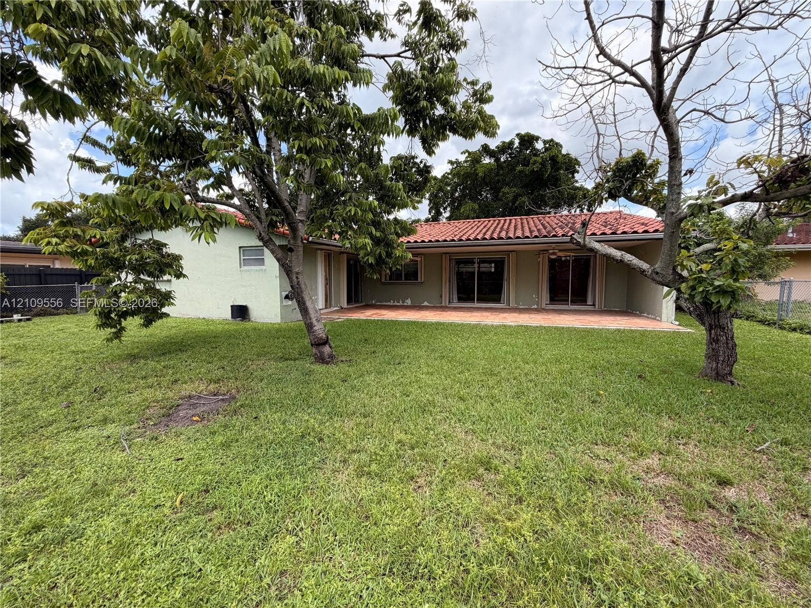 Rear exterior featuring a terracotta tile roof, masonry construction, tiled patio, and mature trees
