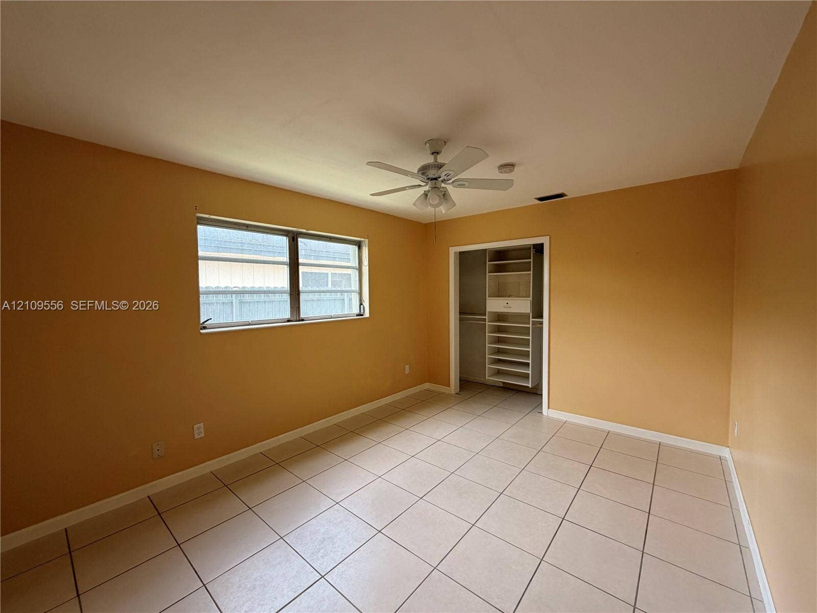 Room featuring tile flooring, multi-pane window, ceiling fan with integrated light fixture, and closet with built-in shelving
