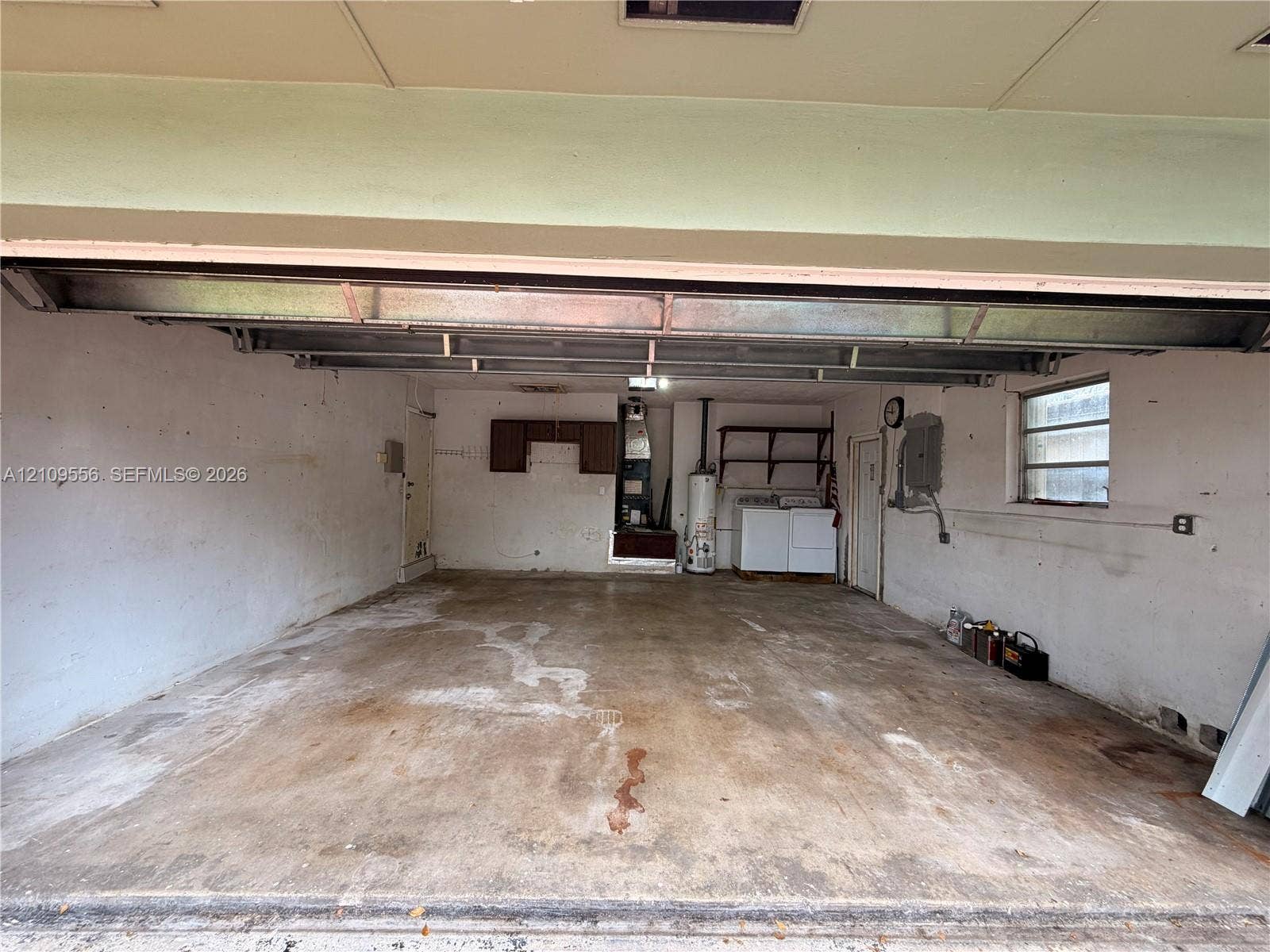 Enclosed two-car garage featuring a concrete floor, built-in wooden wall shelving, a framed window, and a dedicated laundry area with utility hookups