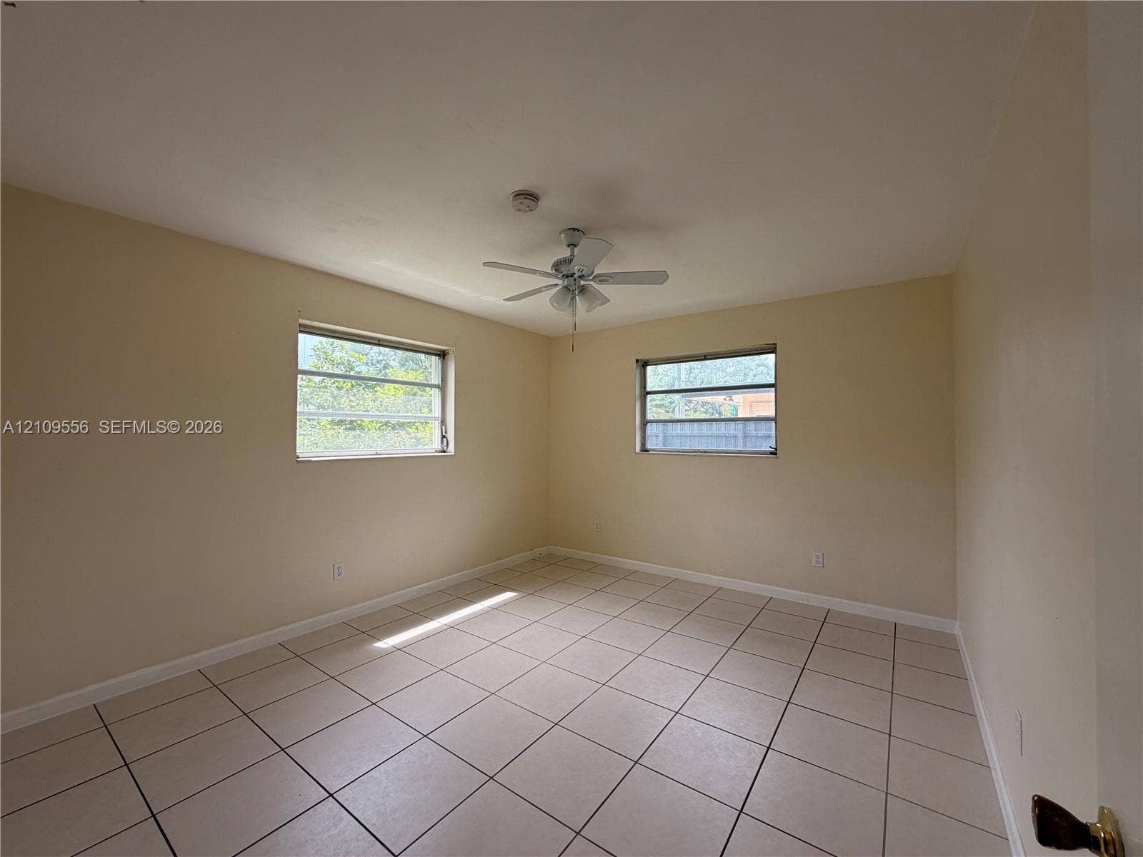 Neutral-toned room featuring large-format ceramic tile flooring, two horizontal sliding windows, and a ceiling-mounted fan with integrated lighting